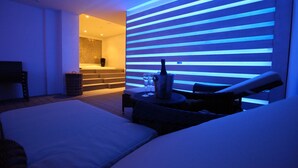 A modern hotel room with a large bed, a seating area with a table, and a wall with horizontal lighting. - Dan Panorama Tel Aviv (Tel Aviv)