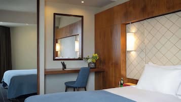A hotel room with two beds, a desk, a chair, a mirror, and a wall-mounted light fixture.