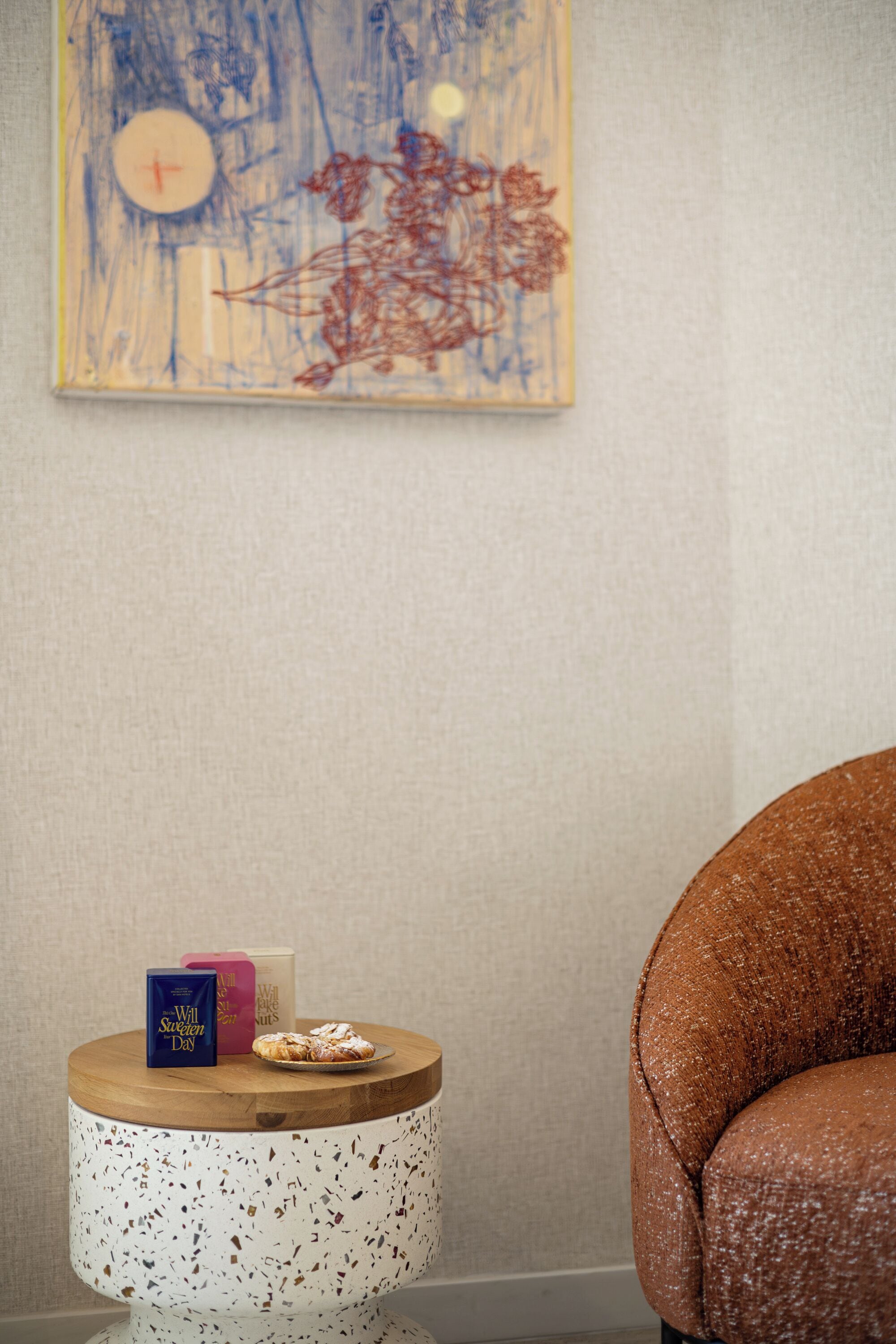 A round wooden side table with a white speckled top, a small blue box, a pink box, and a plate with a pastry.