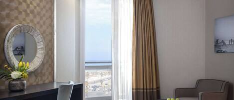 A hotel room with a large window, a desk with a chair, a bed, and a small table with fruit.