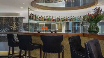 Zona de bar con barra circular, varias botellas de licor y tres taburetes.