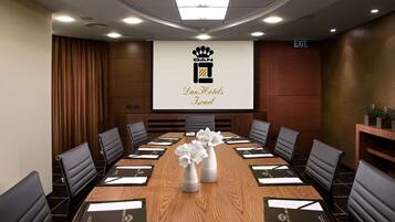Ein Konferenzraum mit einem langen Tisch, schwarzen Stühlen und einer Projektionsleinwand, die 'Dan Hotels Israel' zeigt.