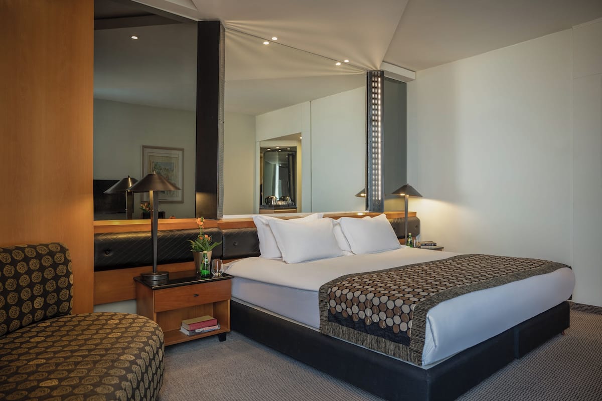A hotel room with a large bed, a nightstand with a lamp, a chair, and a mirror.