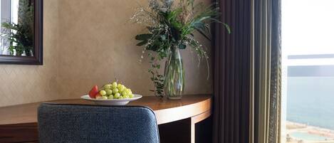 A hotel room with a desk, a chair, a vase with flowers, and a view of the sea.