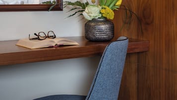A wooden desk with a vase of flowers, a pair of glasses, and an open book.