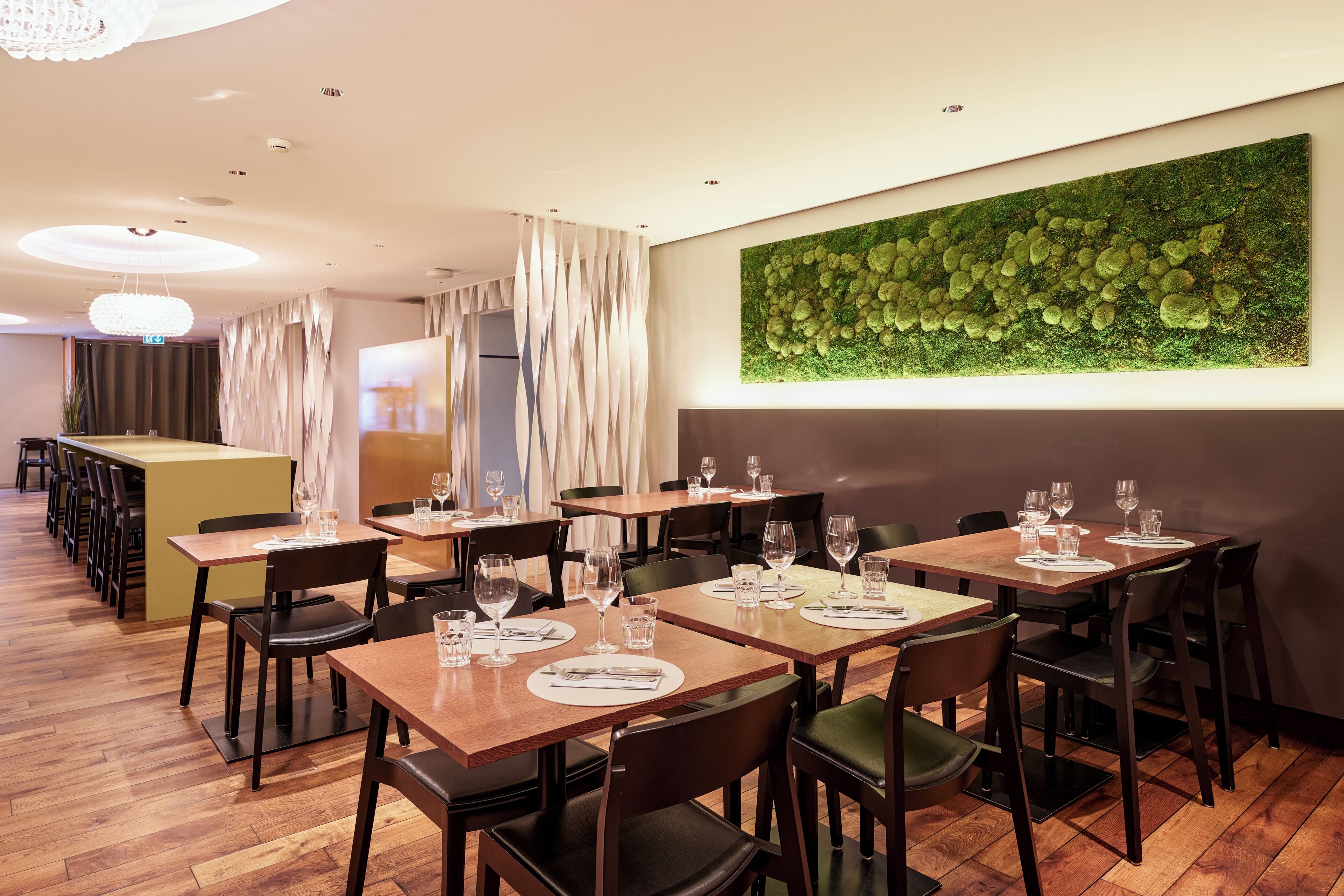 A restaurant with multiple tables, chairs, and a green wall art piece.