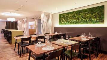 A restaurant with multiple tables, chairs, and a green wall art piece.