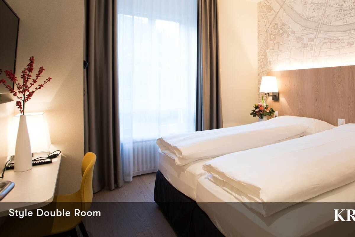 A double room with two beds, a desk with a lamp, a chair, and a map on the wall.
