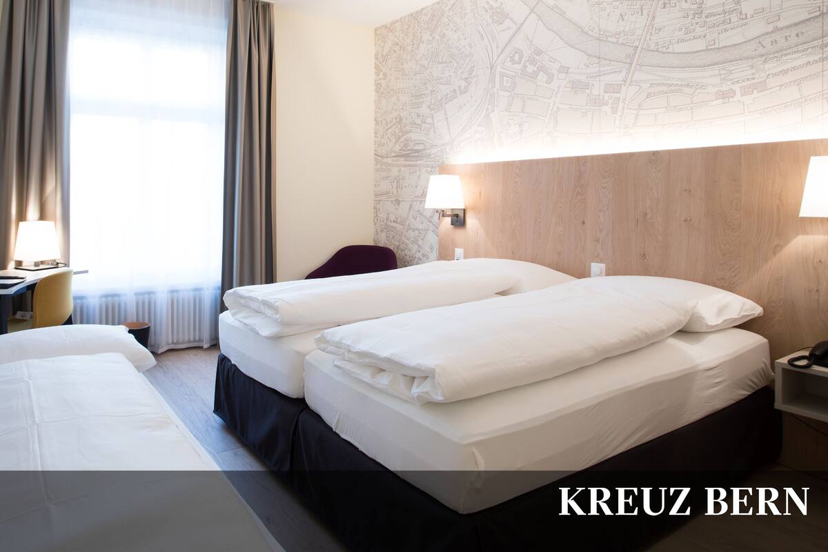 A triple room with two beds, a desk, a chair, a lamp, and a map on the wall.
