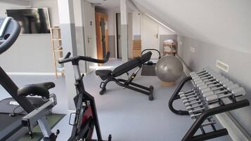 A home gym with exercise equipment including a treadmill, elliptical, stationary bike, and a set of dumbbells.