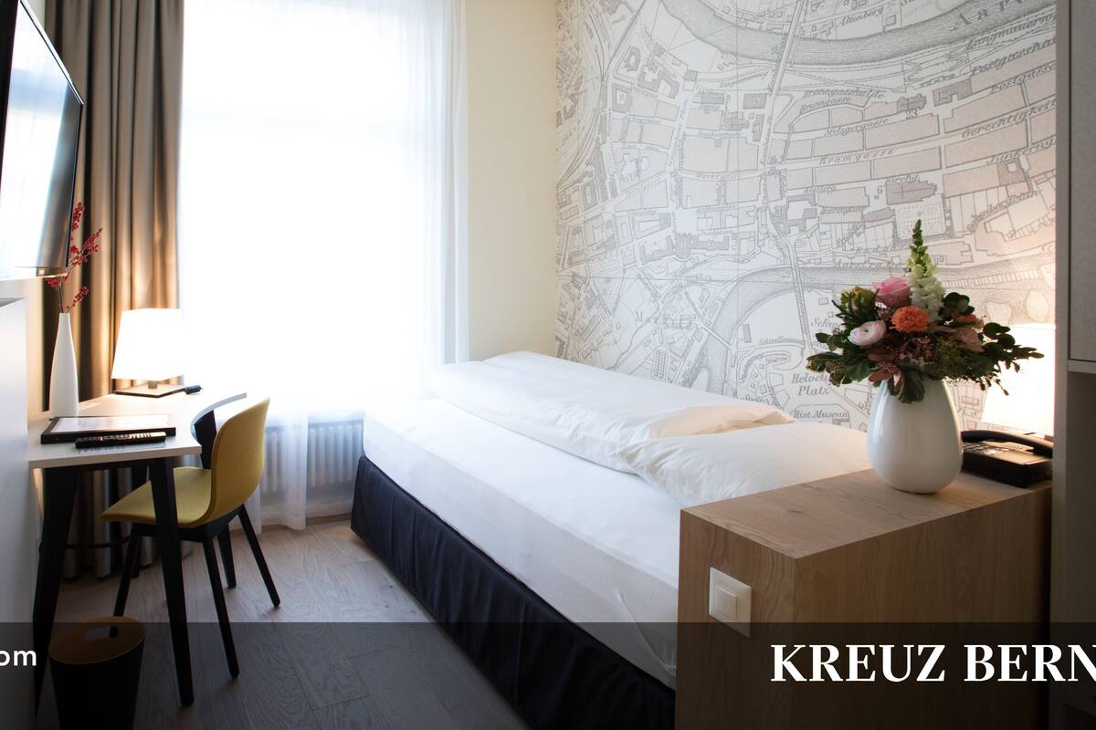 A single room with a bed, a desk, a chair, a TV, and a map on the wall.