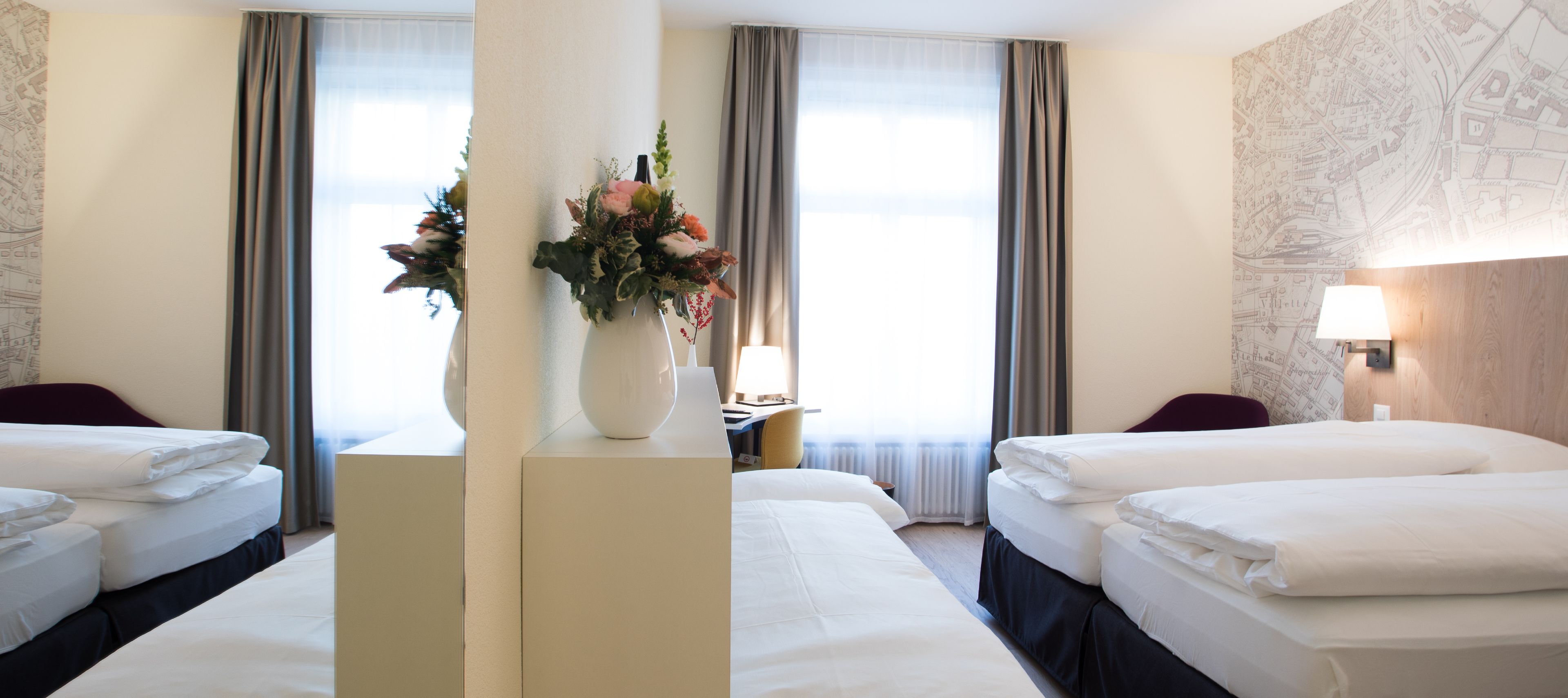 Ein Hotelzimmer mit zwei Betten, einer Blumenvase, einer Lampe und einer Karte an der Wand.
