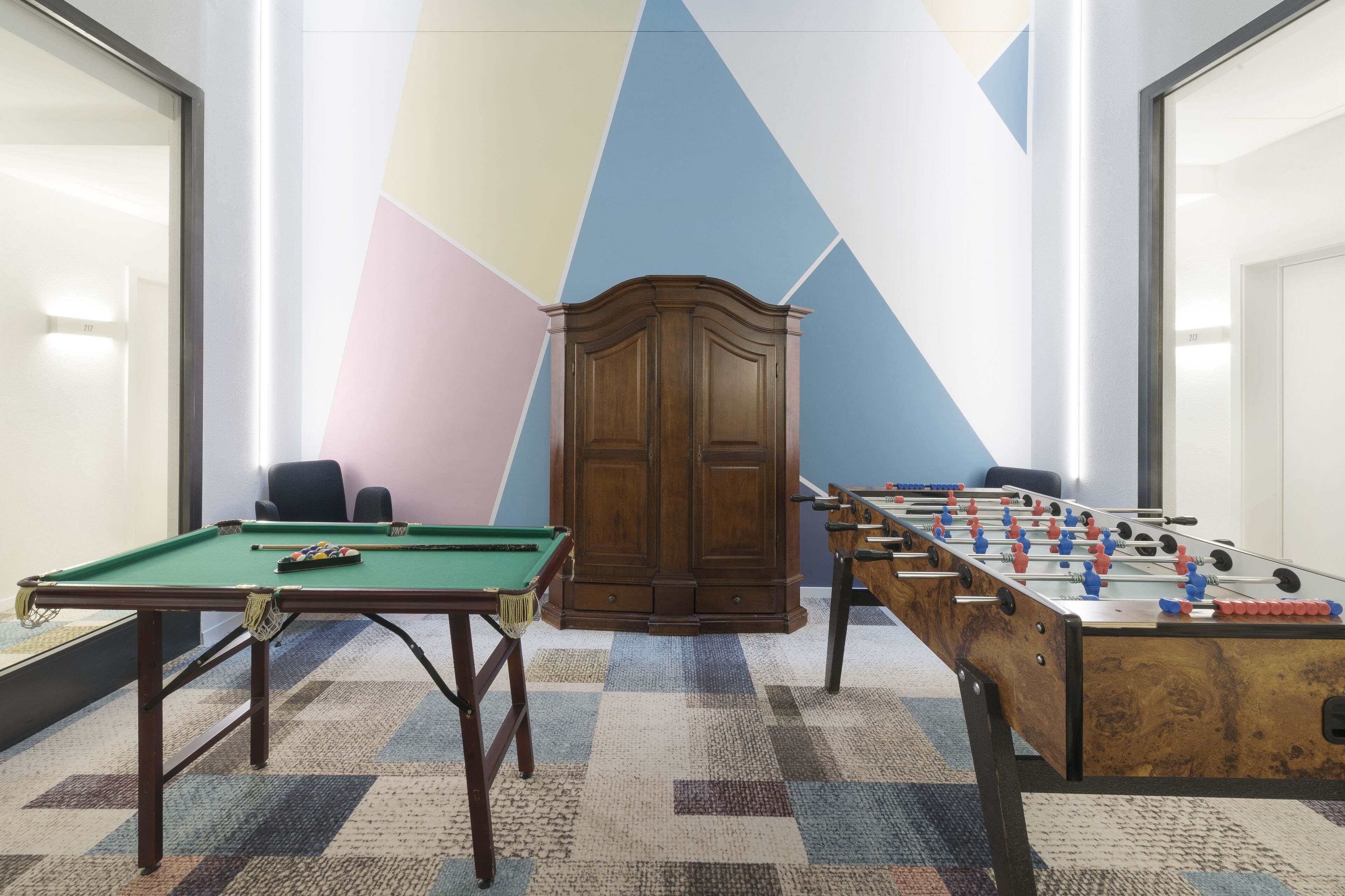 A room with a pool table, a foosball table, and a cabinet.