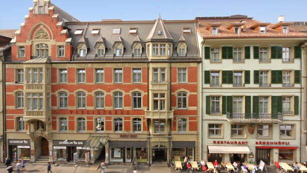 Une rangée d’immeubles à étages multiples, avec différentes boutiques en rez-de-chaussée, dont un restaurant et une librairie.