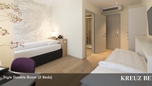 Une chambre double avec deux lits, un bureau, une chaise, une carte accrochée au mur et un appareil de climatisation.