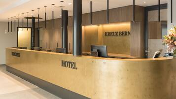 Ein Hotelrezeptionsschalter mit Holzvertäfelung, einem 'KREUZ BERN'-Schild und einer Blumenkomposition.