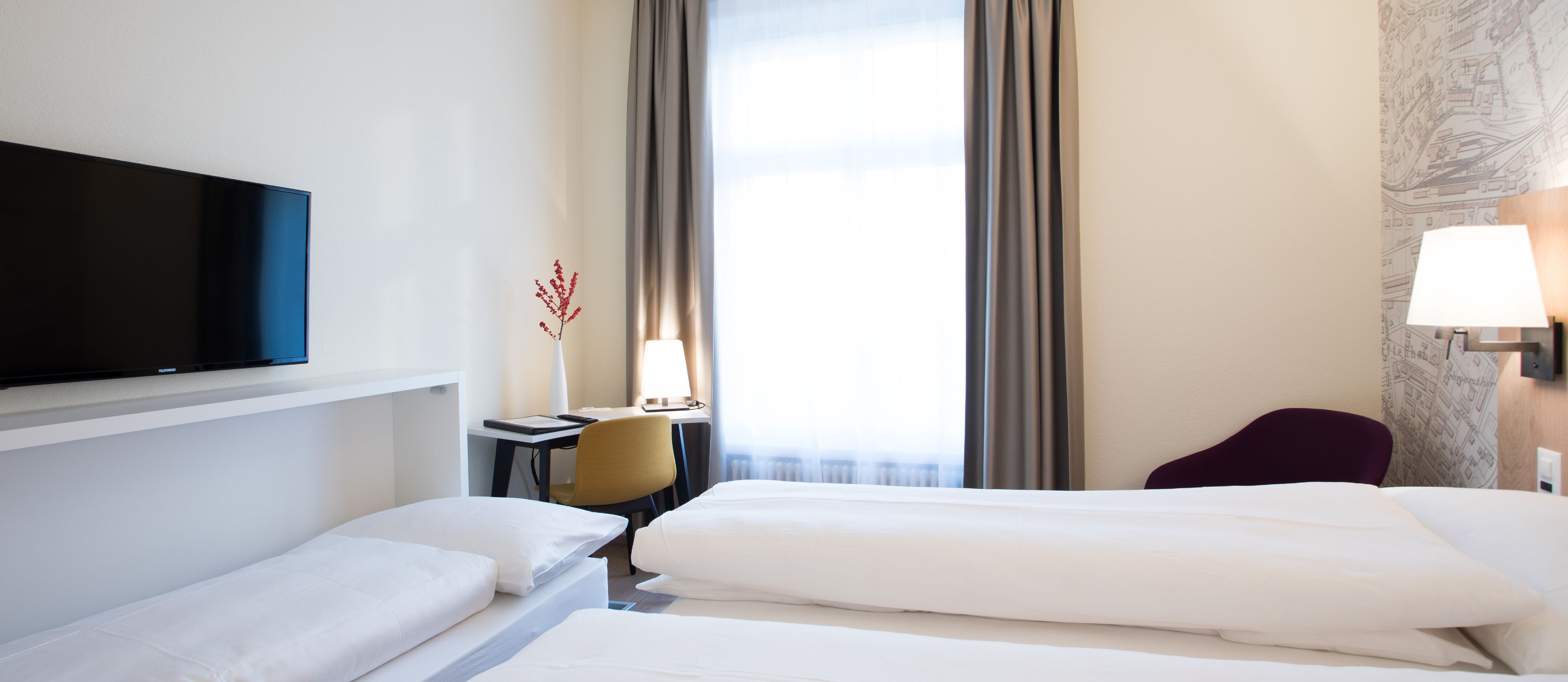 A hotel room with two beds, a desk, a chair, a TV, and a window with curtains.