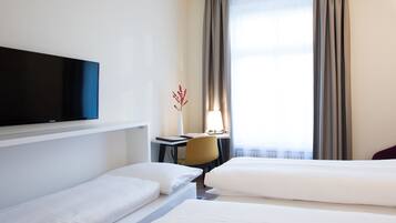 A hotel room with two beds, a desk, a chair, a TV, and a window with curtains.