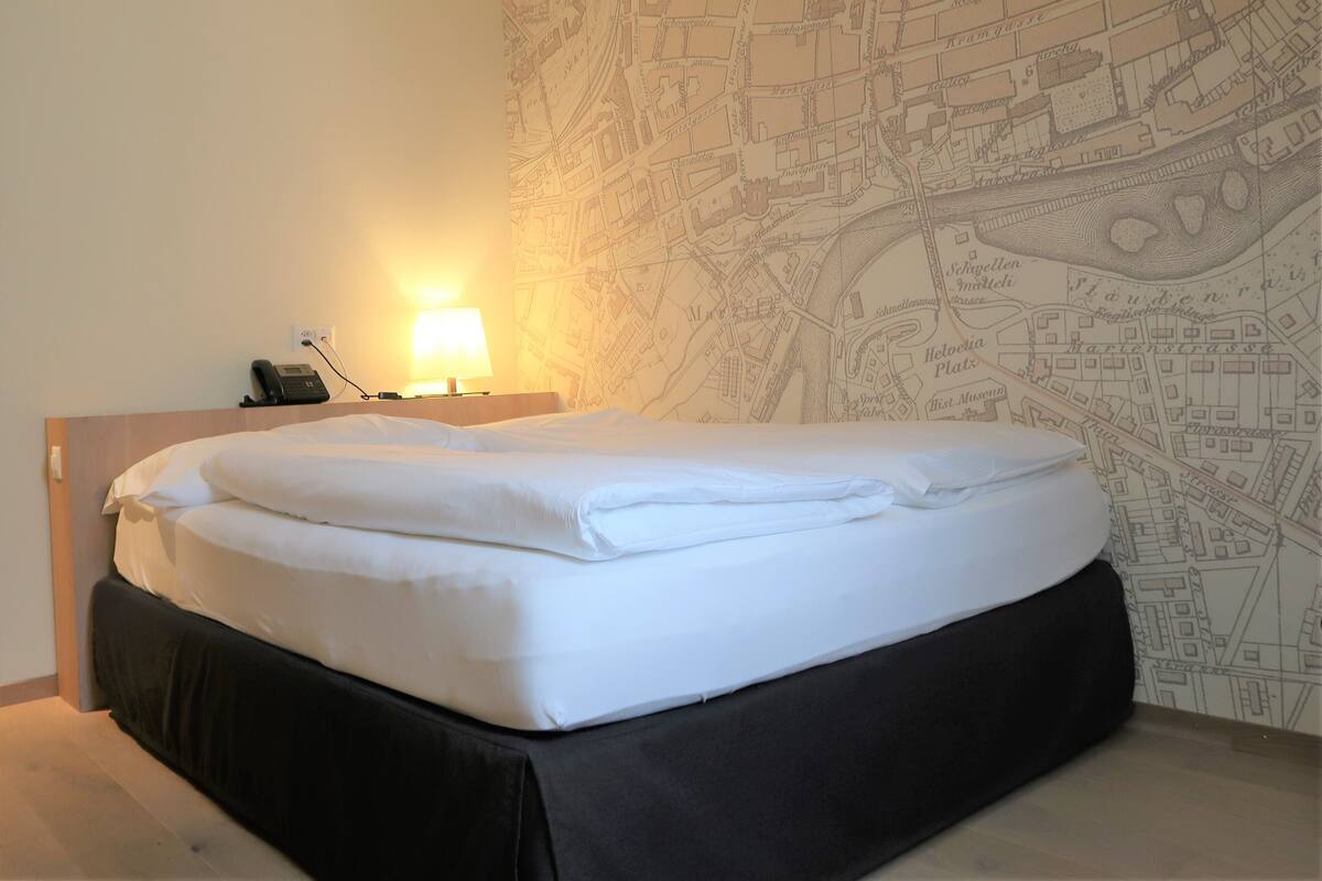 A neatly made bed with white linens, a bedside lamp, and a wall map.