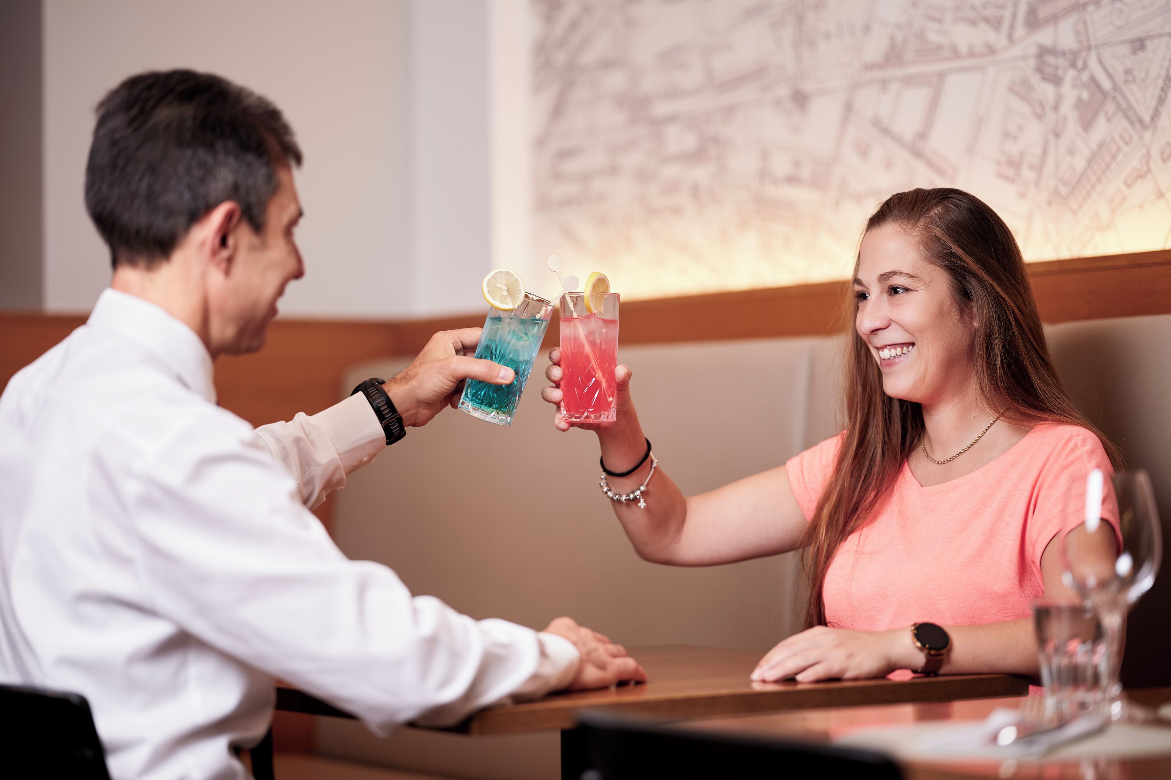 Un hombre y una mujer sentados a una mesa con bebidas, un reloj y una pulsera a la vista.