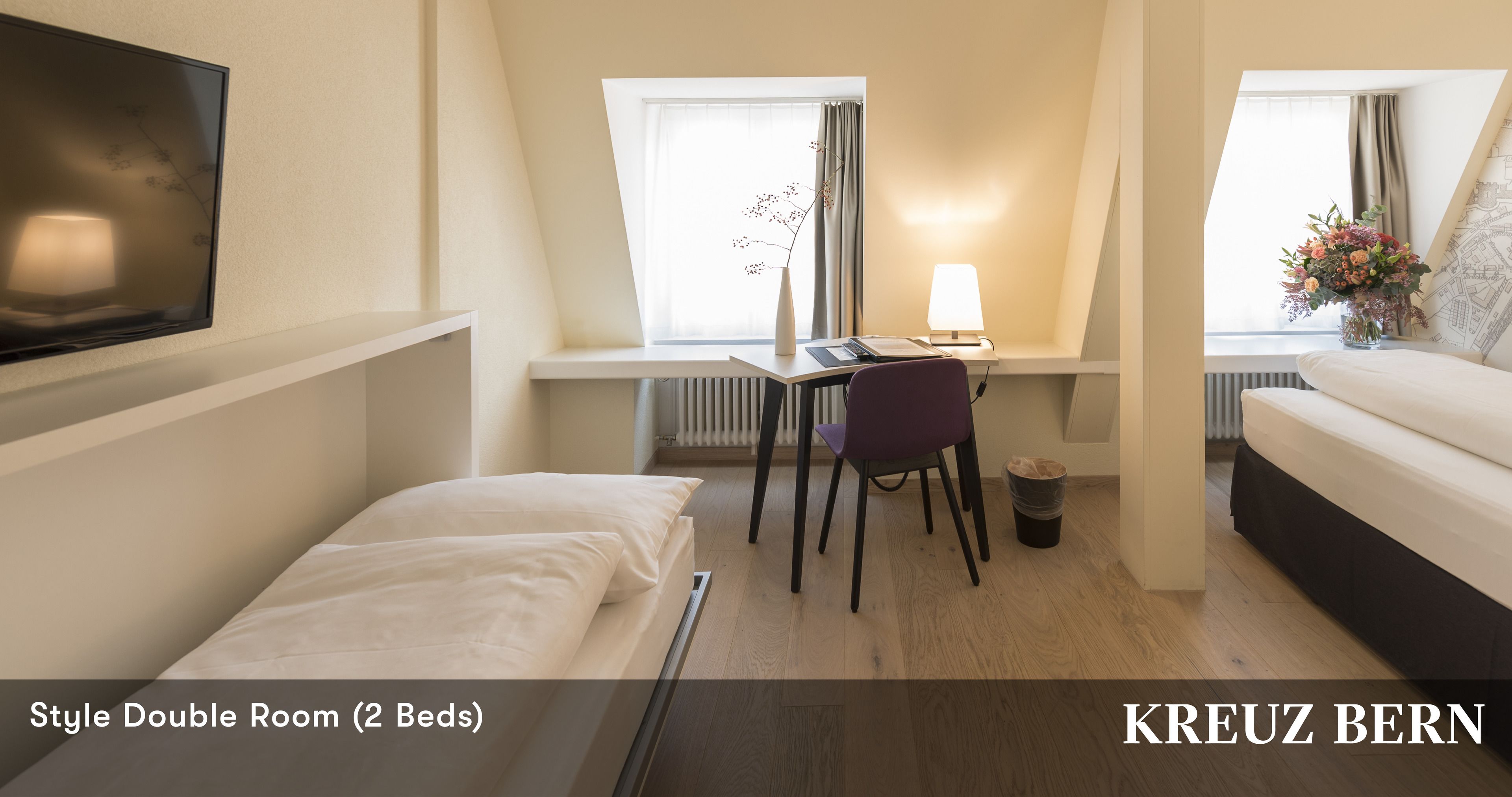 A double room with two beds, a desk with a chair, a TV, and a window with curtains.