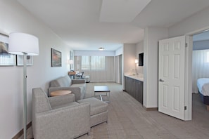 A hotel room with a sofa, a small table, a desk with a chair, a TV, and a door leading to a bathroom. - Holiday Inn Palmdale-Lancaster by IHG (Palmdale)