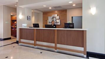 A hotel reception desk with a wooden counter, a digital screen, and a sign that reads "Holiday Inn."