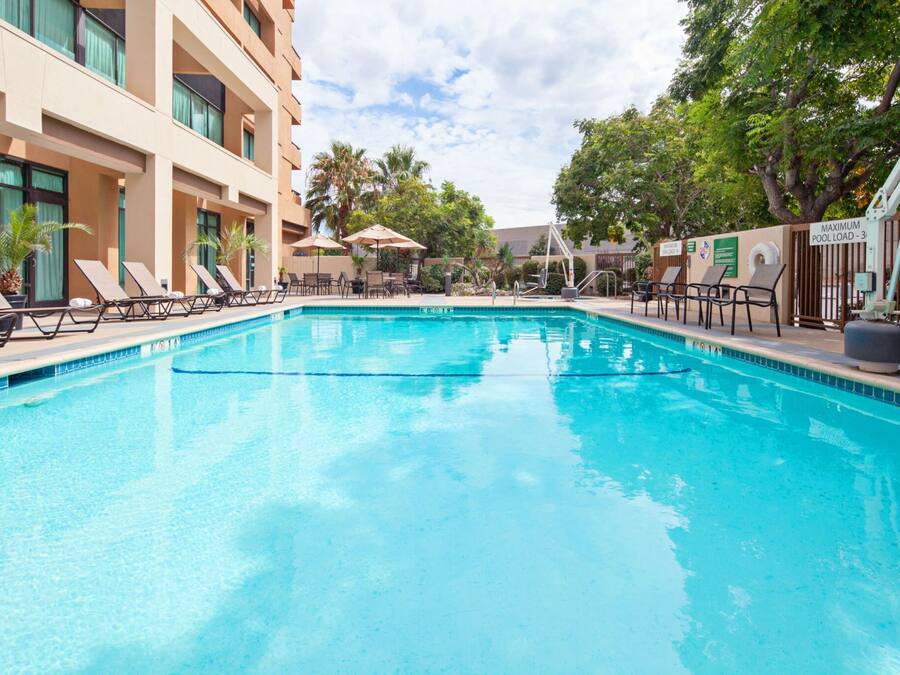 A swimming pool with lounge chairs and umbrellas, surrounded by a building with multiple floors and windows.