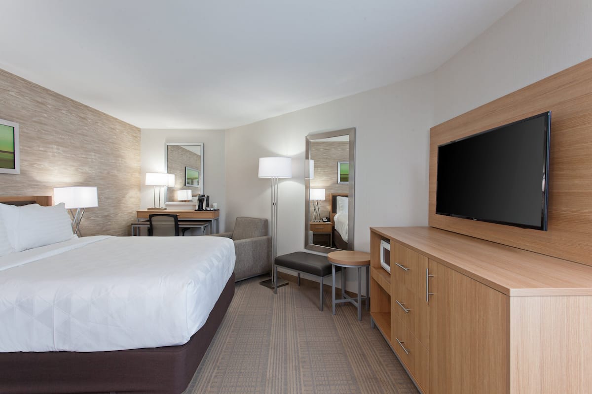 A hotel room with a large bed, a desk with a chair, a small table, a TV, and a wardrobe.