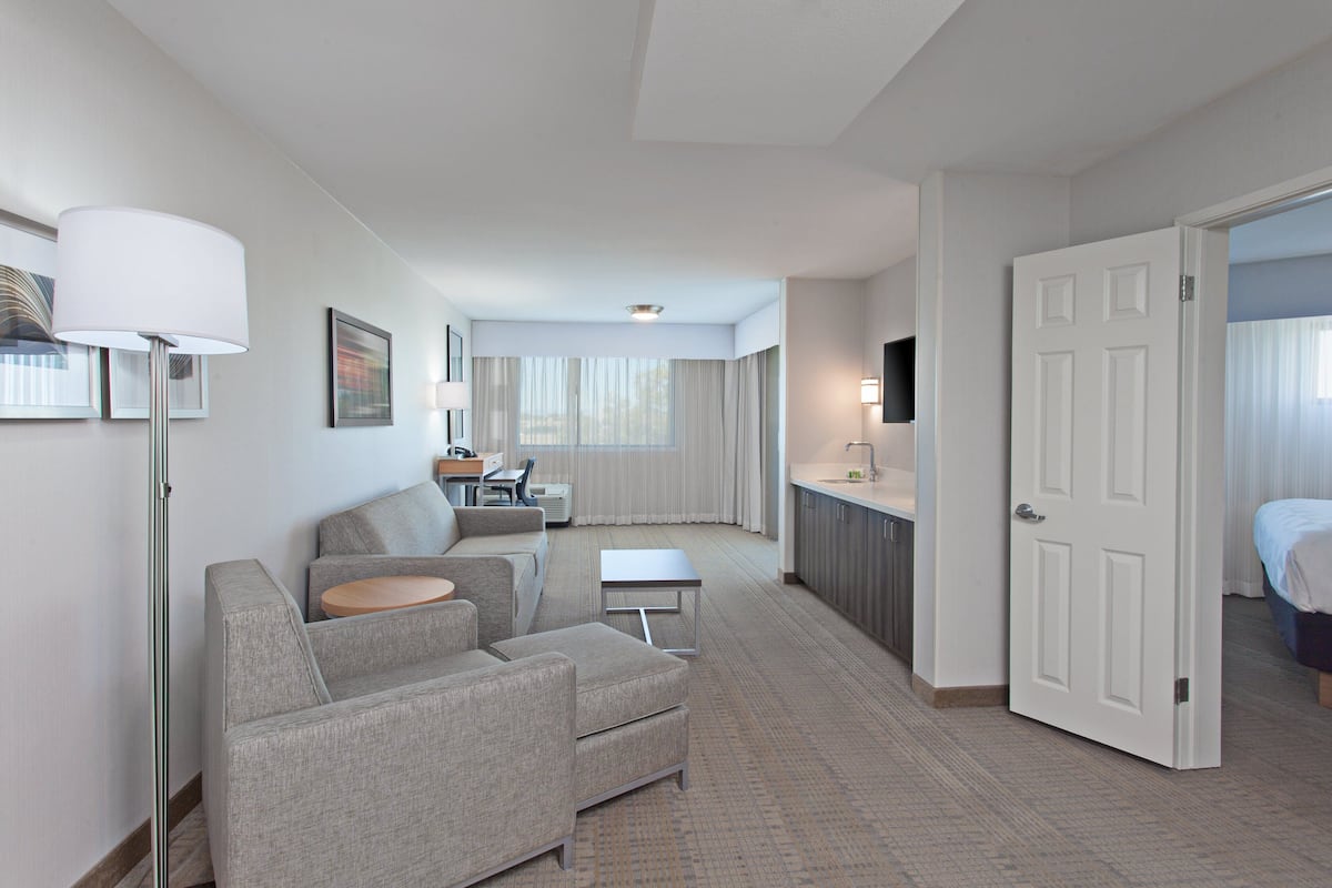 A hotel room with a sofa, a small table, a desk, a TV, and a door leading to a bathroom.