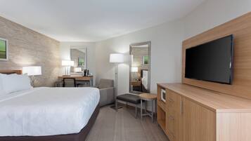 A hotel room with a large bed, a desk, a chair, a TV, and a wardrobe.