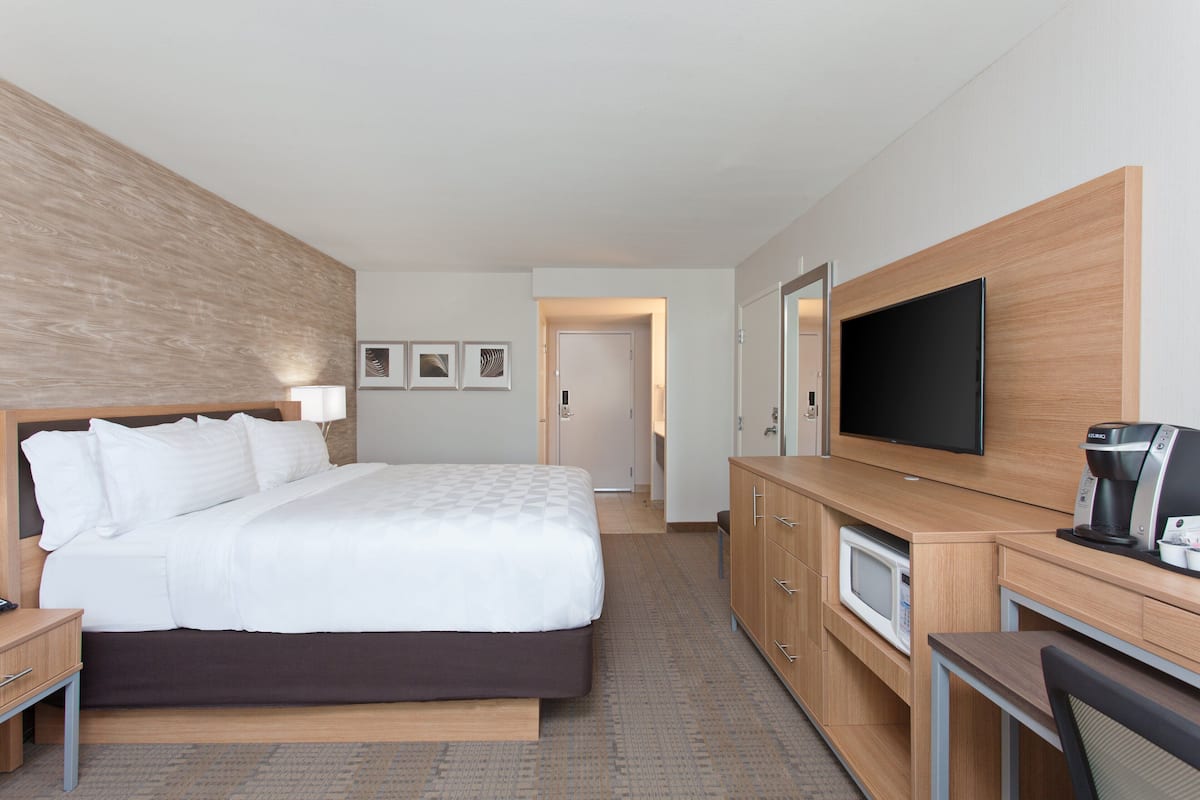 A modern hotel room with a large bed, a flat-screen TV, a microwave, and a coffee maker.