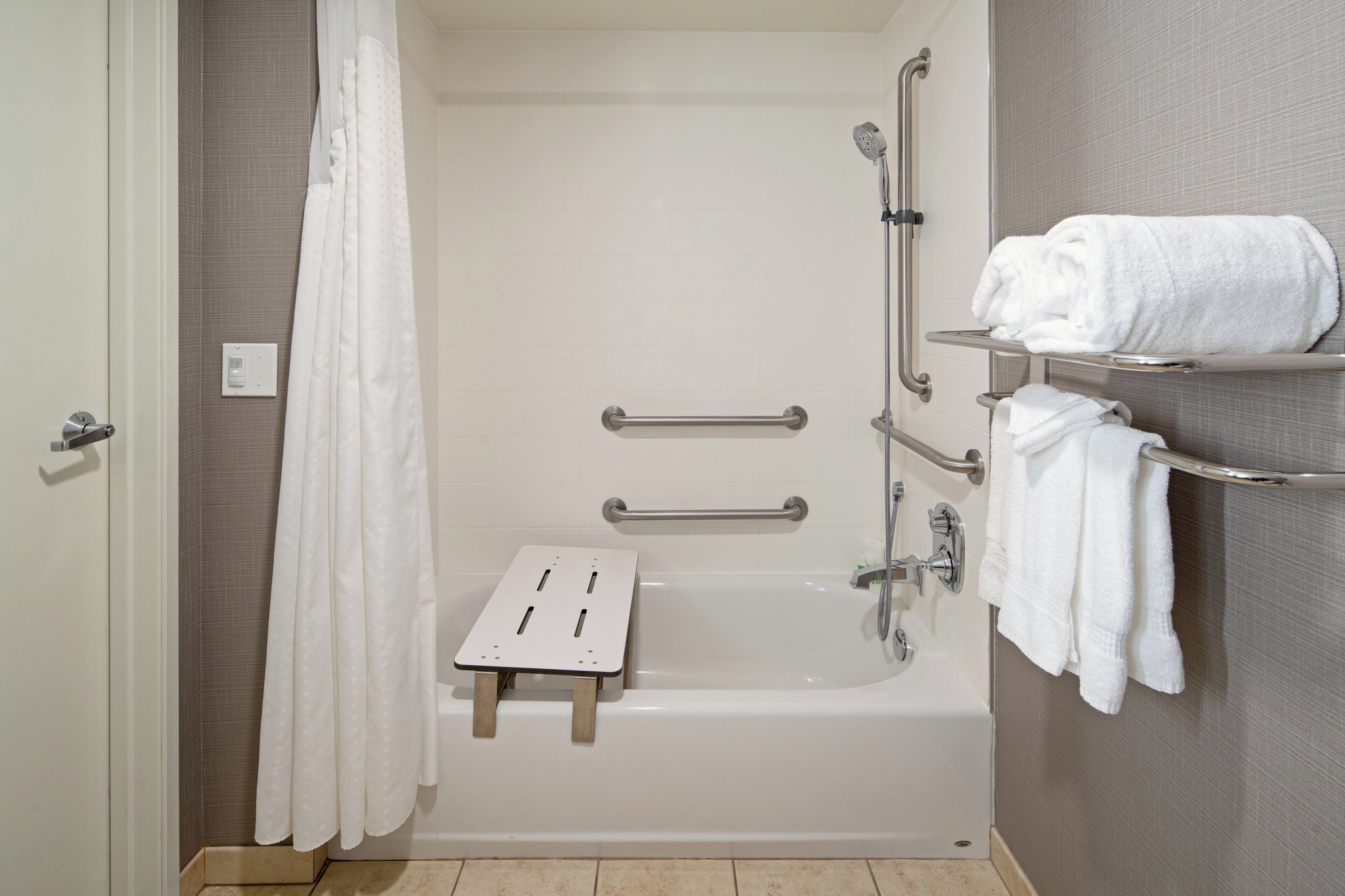 A bathroom with a bathtub, grab bars, a shower seat, and a towel rack.