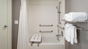 A bathroom with a bathtub, grab bars, a shower seat, and a towel rack. - Holiday Inn Palmdale-Lancaster by IHG (Palmdale)