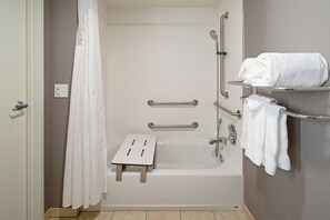 A bathroom with a bathtub, grab bars, a shower seat, and a towel rack.