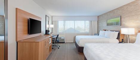 A hotel room with two beds, a desk, a TV, and a window with curtains.
