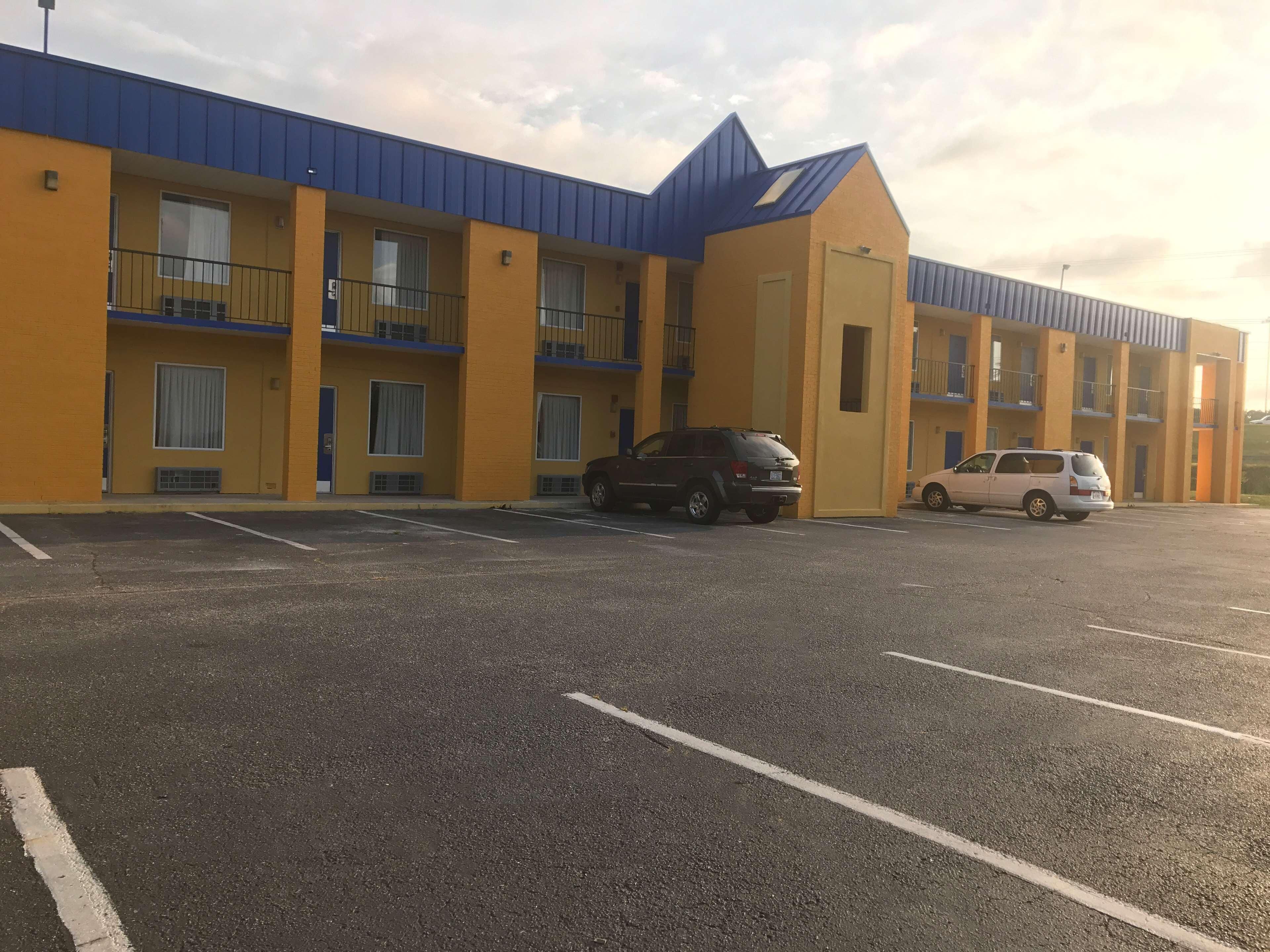 Un motel à plusieurs étages, avec un toit bleu et des murs jaunes, et un parking où sont garées plusieurs voitures.