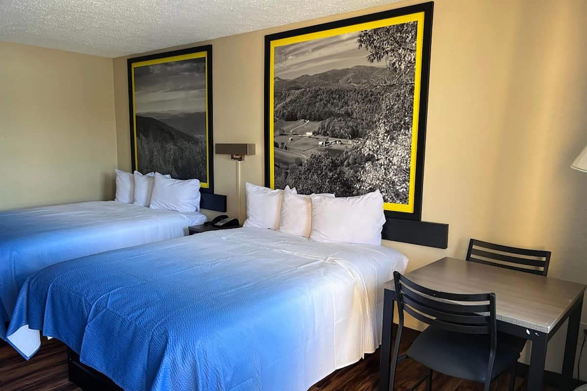 A hotel room with two beds, a desk, and chairs.