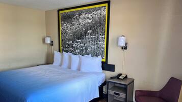 A hotel room with a bed, a nightstand with a phone, a chair, and a large black-and-white floral artwork on the wall.