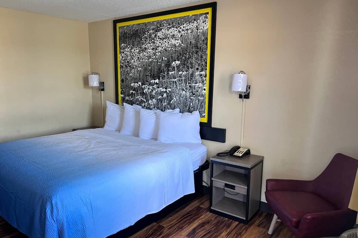 A hotel room with a bed, bedside table, chair, and a large black and white photograph on the wall.