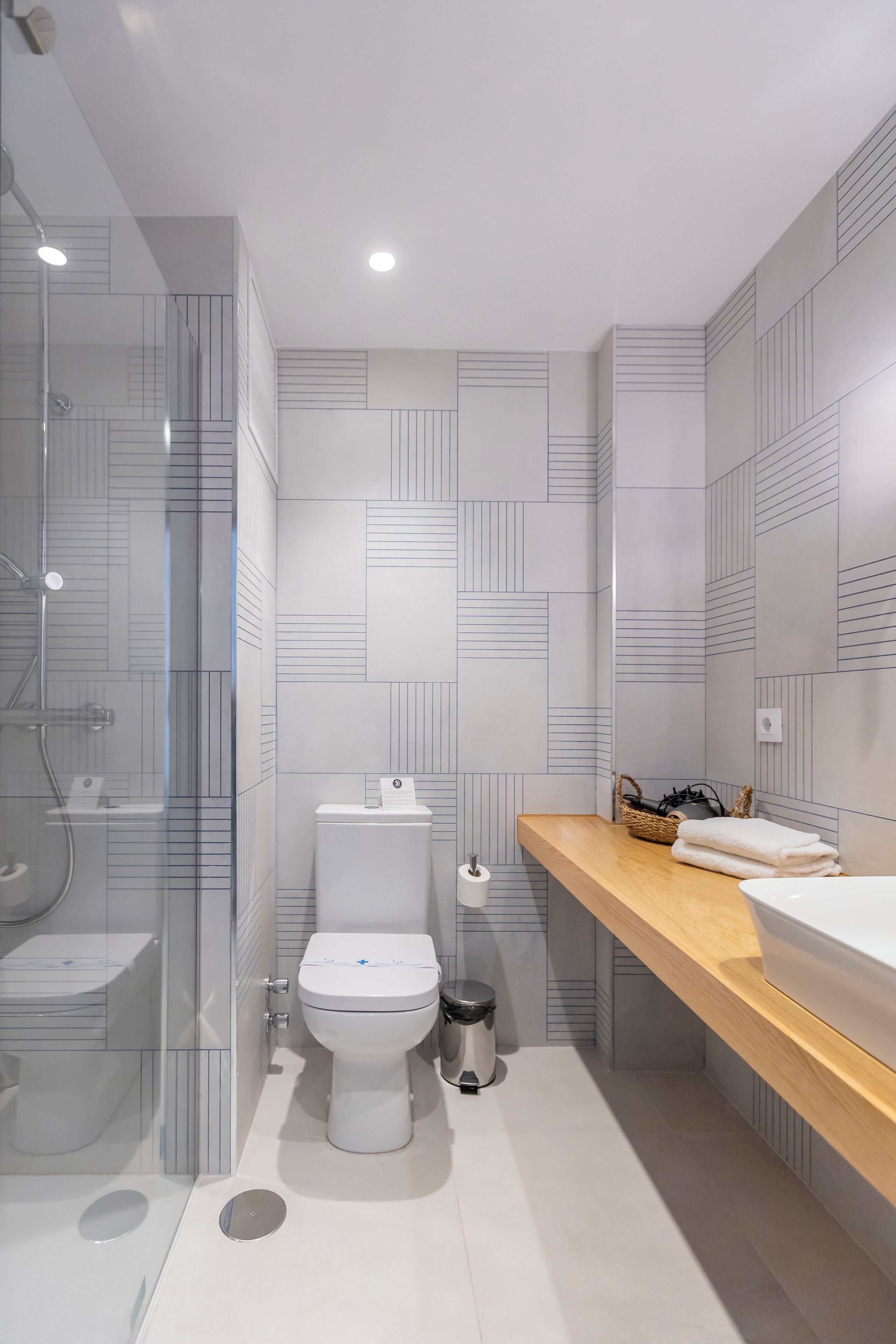 Et moderne badeværelse med glasbrusekabine, toilet og vask med træbordplade.