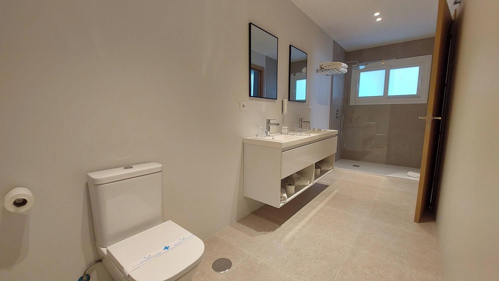 Un baño moderno con inodoro, lavamanos, ducha y espejo.