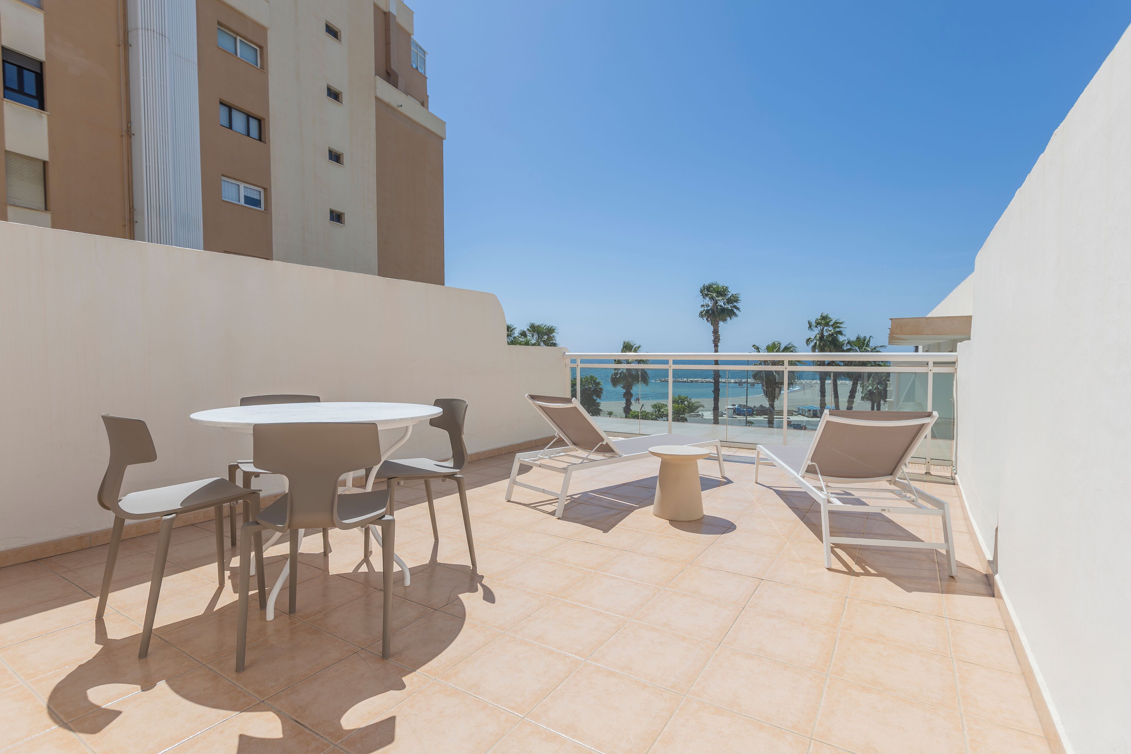 A rooftop terrace with a round table and chairs, a small round table, and lounge chairs.