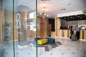 Un hall d’hôtel comprenant un comptoir d’accueil, un espace salon et un mur en verre orné d’un logo.