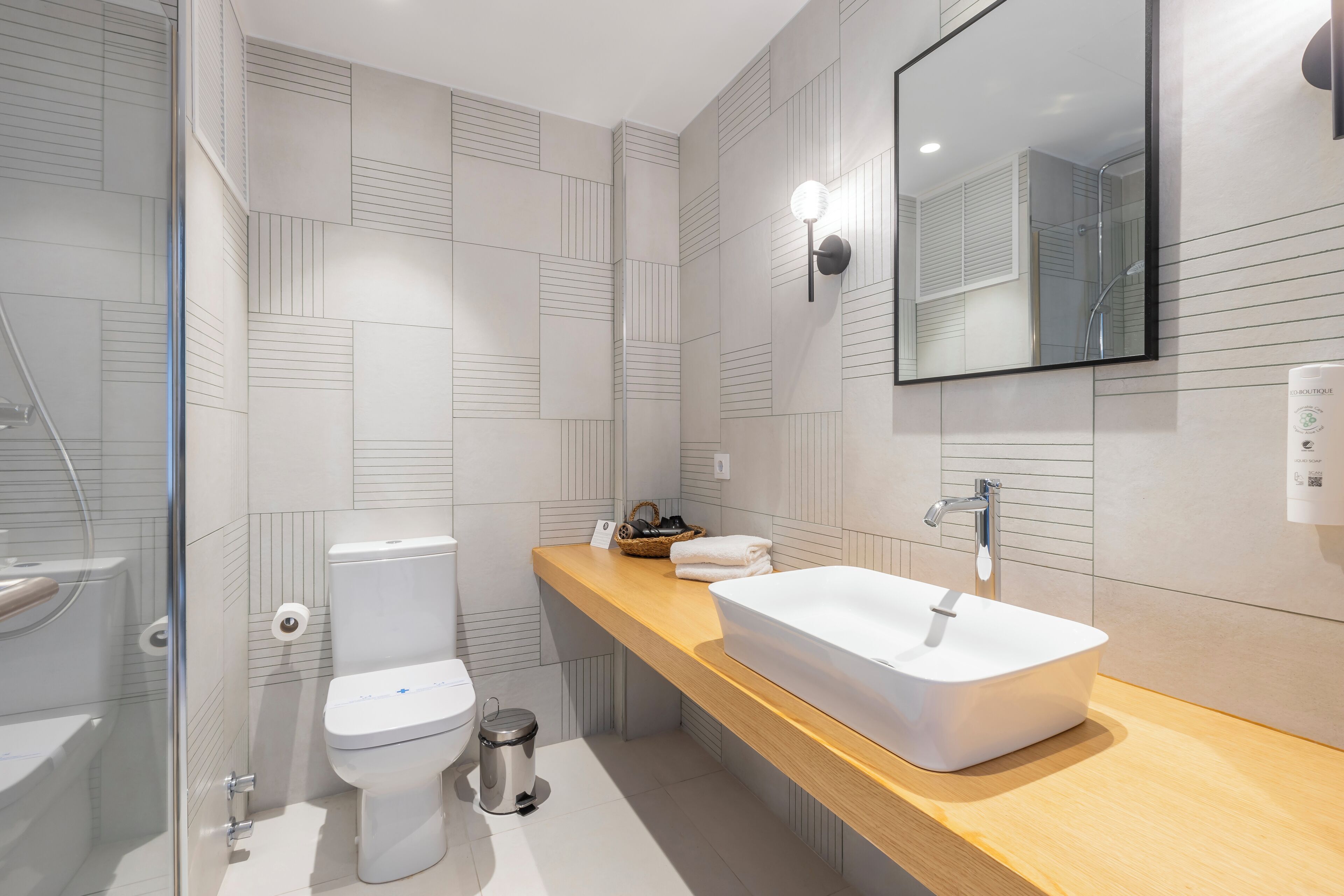 Un baño moderno con un lavamanos blanco, encimera de madera y un espejo grande.