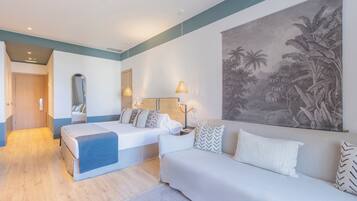 A modern hotel room with a large bed, a sofa, a desk, and a large tropical mural on the wall.