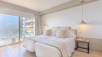 A hotel room with a large balcony, two beds, a bedside table with a phone, and a hanging light fixture.