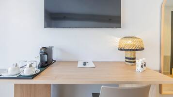 Hotelkamer met een houten bureau, een koffiezetapparaat, een dienblad met kopjes en schotels, een lamp en een spiegel.