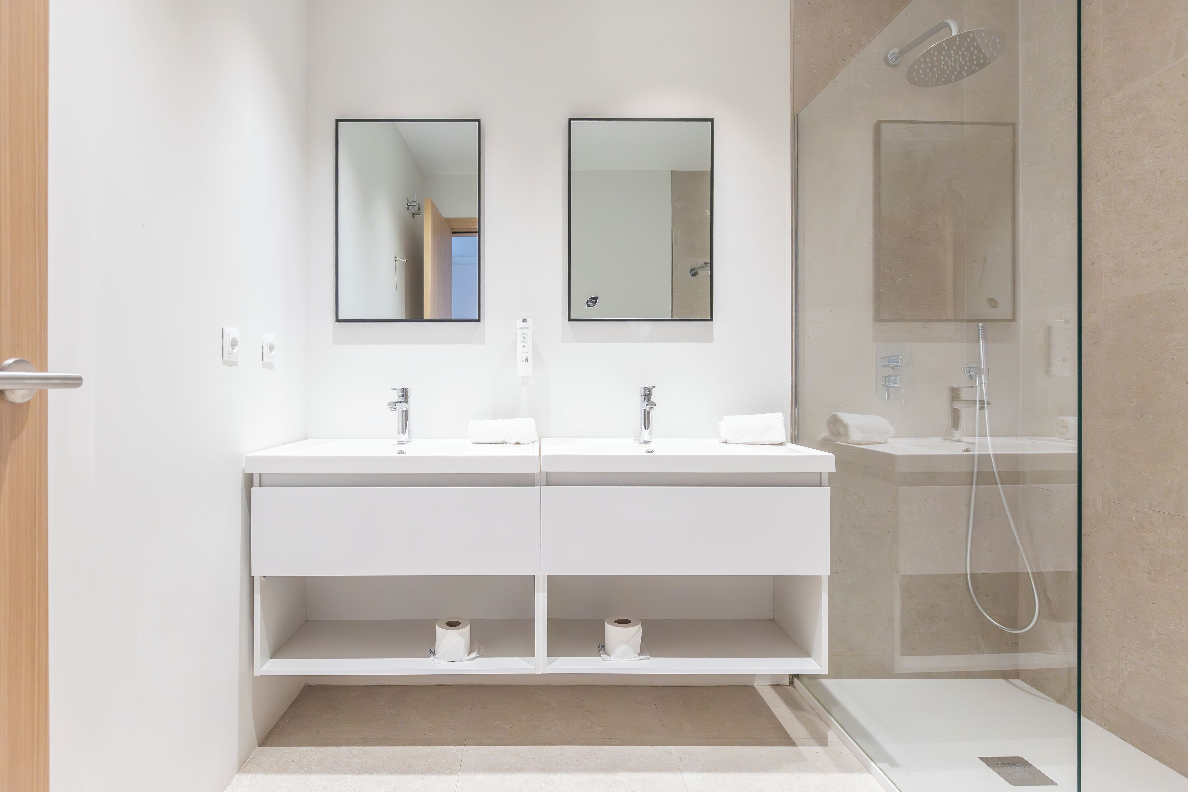 Ein modernes Badezimmer mit zwei Waschbecken, einer Duschkabine aus Glas und einem Spiegel über den Waschbecken.