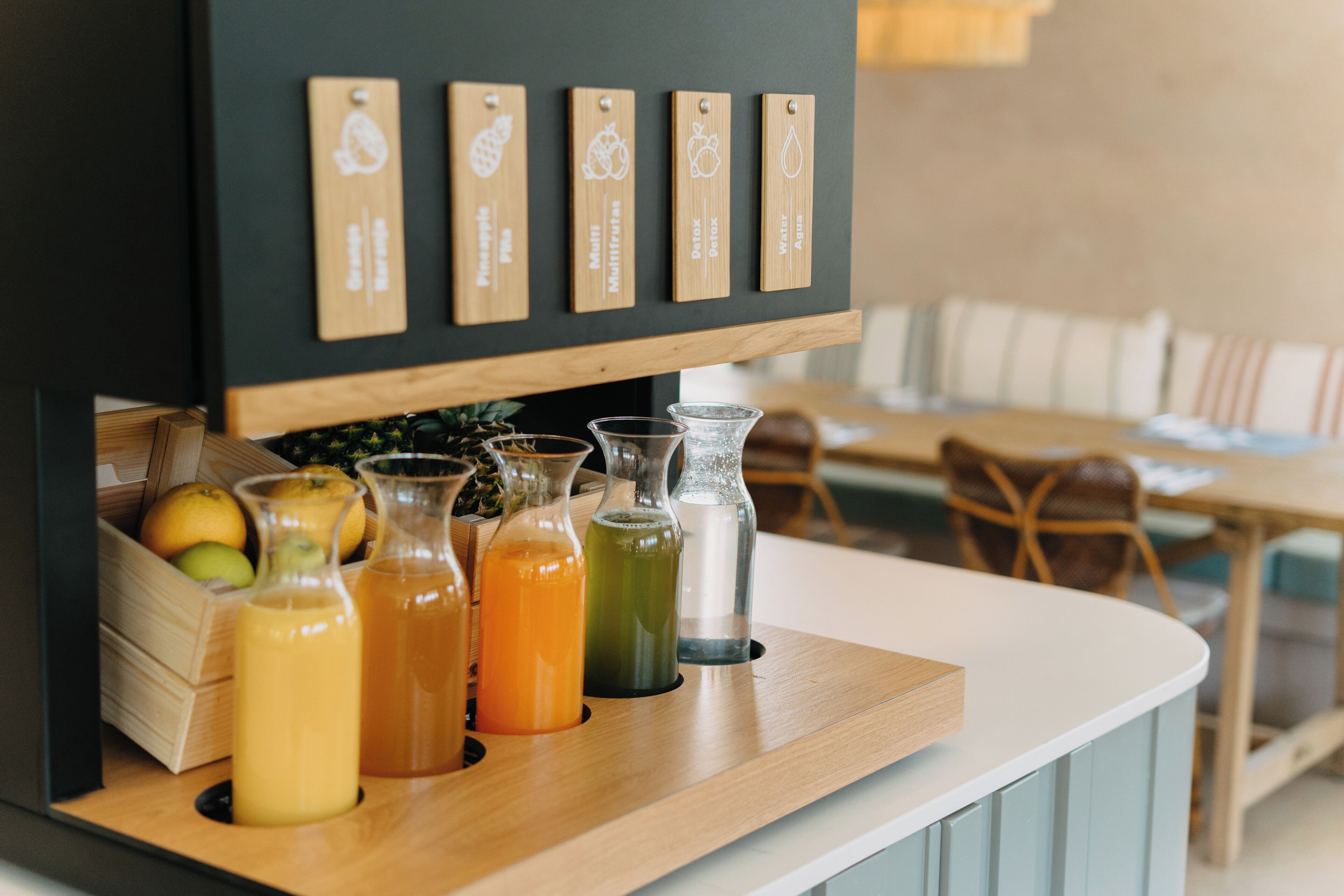 A bar area with wooden shelves displaying various drink options and a wooden counter with glasses of different colored beverages.